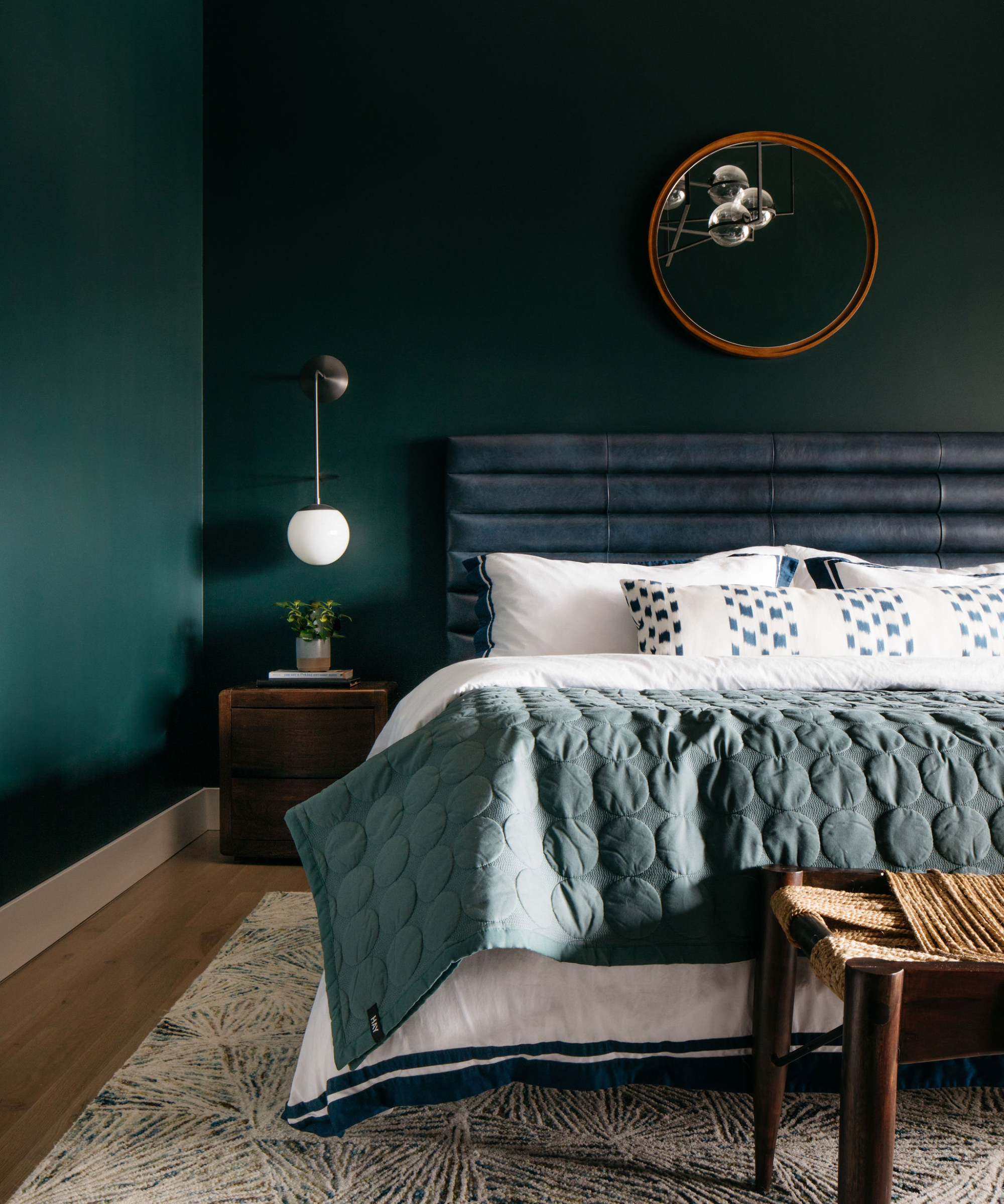 dark green bedroom with emerald walls, hardwood floor, rug, upholstered headboard, white bedding, green throw, round mirror