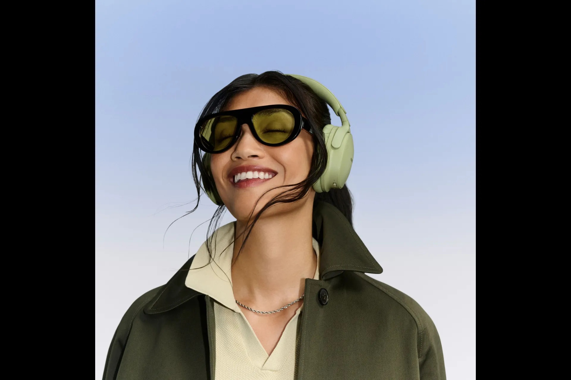 Vrouw met bril en de Bose QuietComfort Headphones (2e gen) in eucalyptusgroen