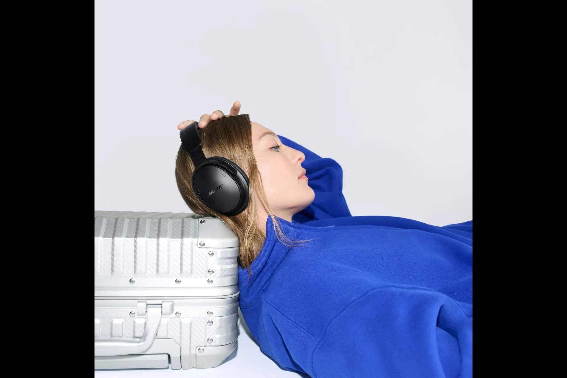Vrouw rust met de Bose QuietComfort Headphones (2e gen) tegen een koffer