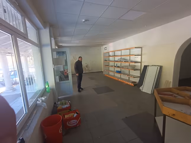 Mann in einem großen, fast leeren Raum mit Regalen an der Wand und großen Fenstern auf der linken Seite.