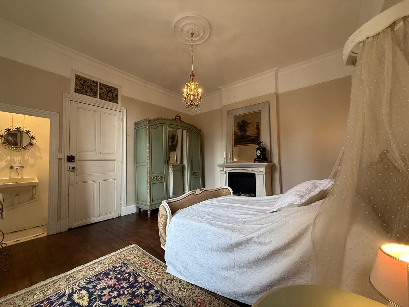 Helles Schlafzimmer mit großem Bett mit weißer Tagesdecke, Baldachin, antikem grünen Kleiderschrank mit Spiegel und Kronleuchter.