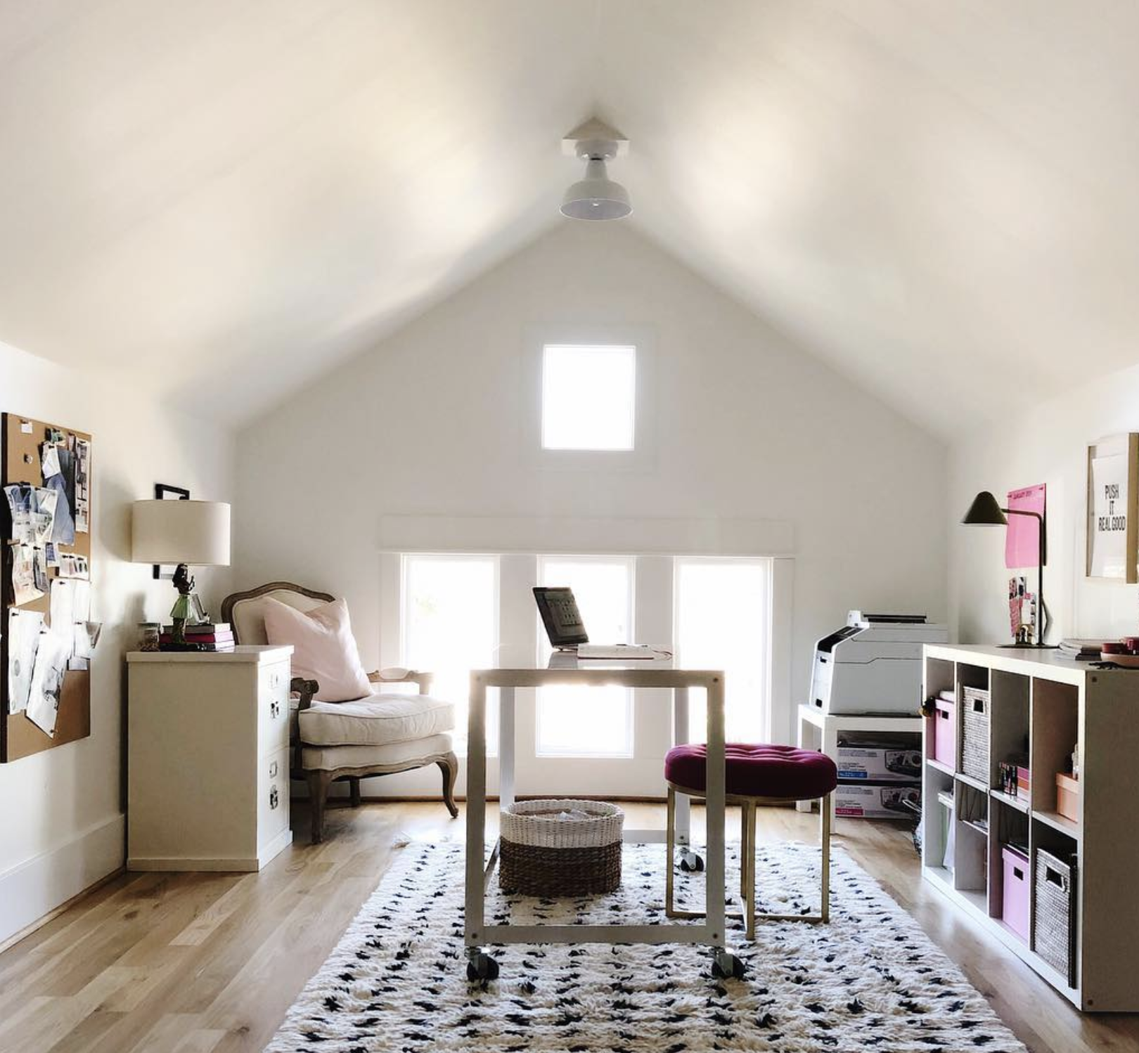 This well lit studio apartment lets in natural light from windows on the far wall. The ceiling angles up like a roof in this cozy studio space.