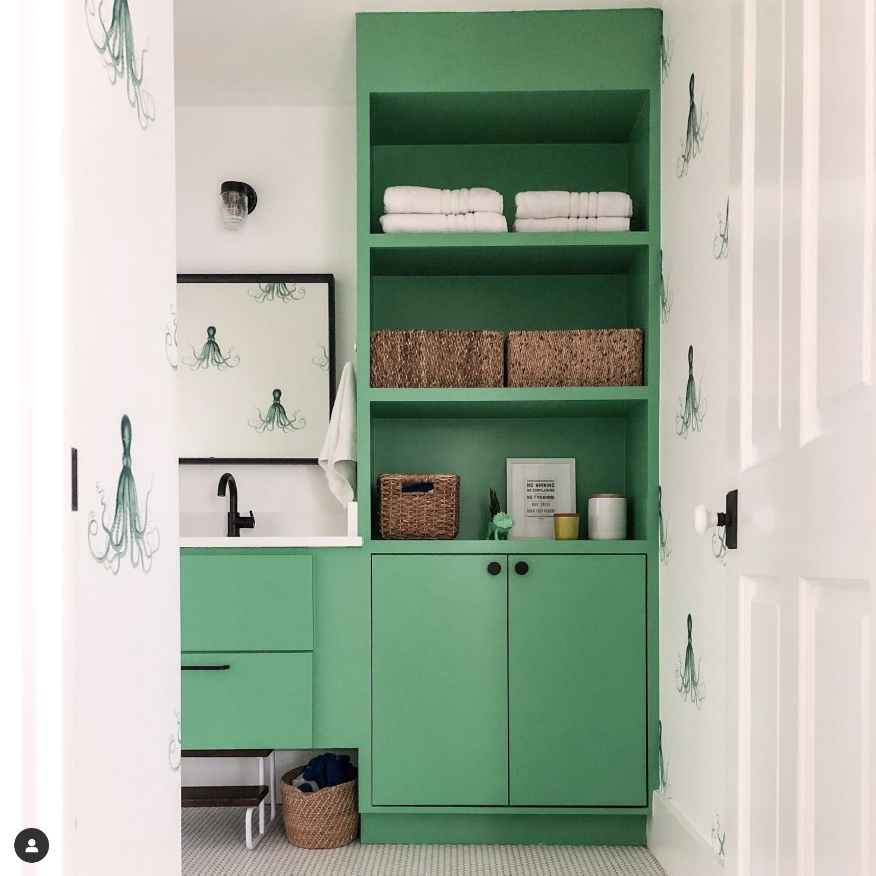 The cabinetry of this bathroom is a lovely bright yet subdued lime green that is accented by white doors and wallpaper that have an elegant and simple nautical pattern.