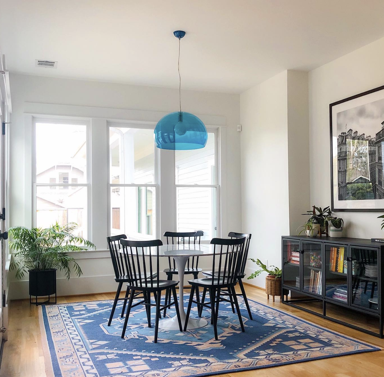 This dining area features a glass, blue light fixture above the centered table with a gorgeous rug underneath.