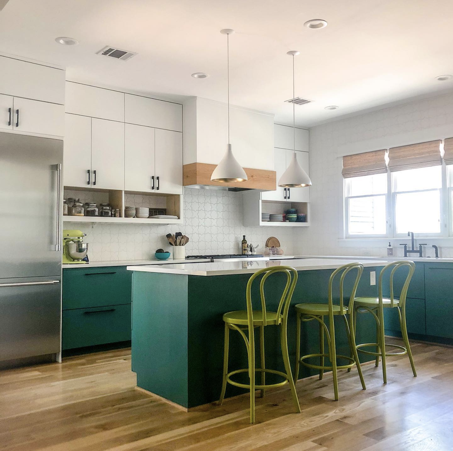 This renovated kitchen features gorgeous olive green bar chairs that compliment the bright forest green island and cabinetry from the waist down. White counter tops and white cabinetry at arms length split the room in half and balance the space.