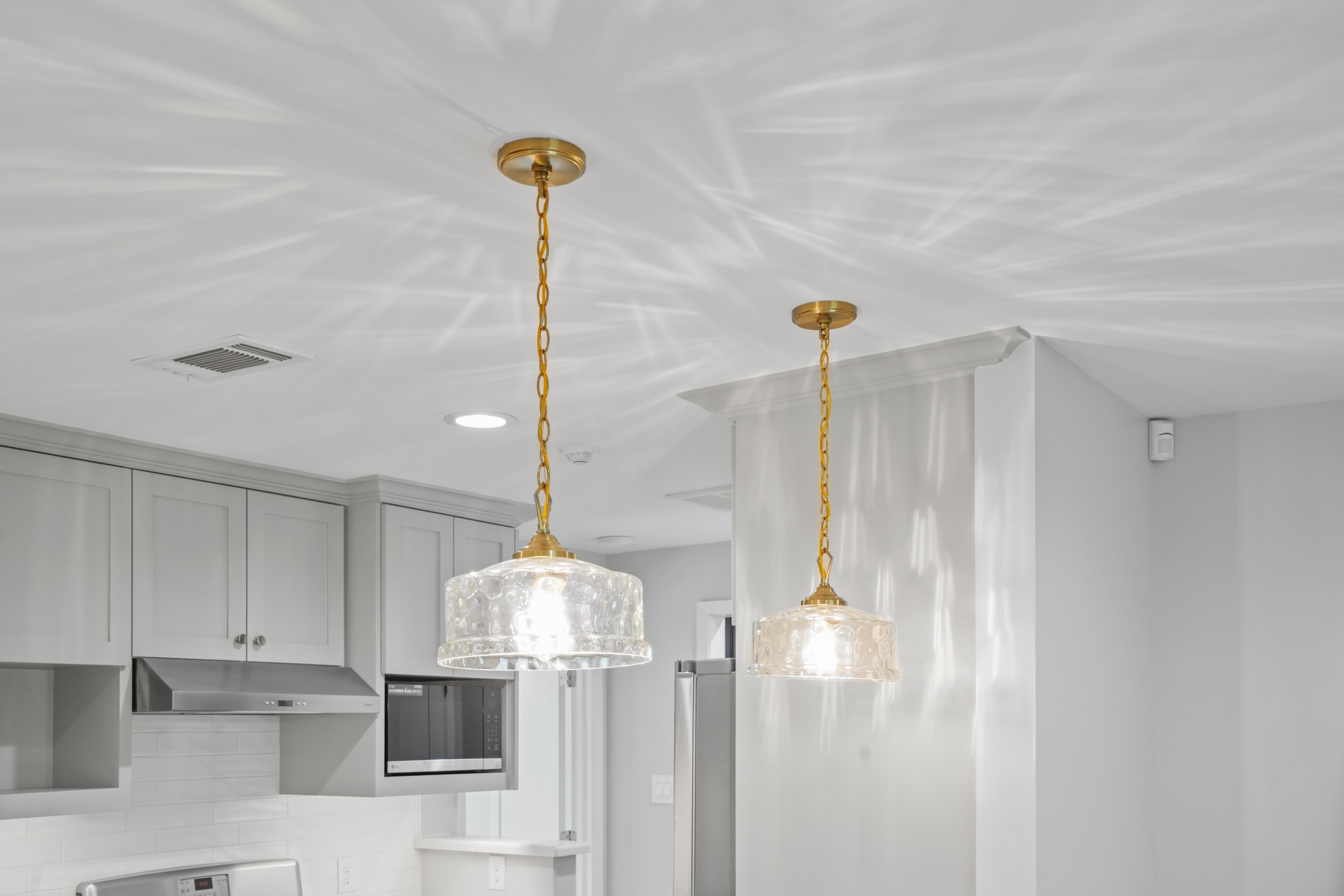This detail shot of the overehad lights in this renovated kitchen add a splash of color with the golden chain that hangs from the ceiling, holding the glass enveloped light bulbs.
