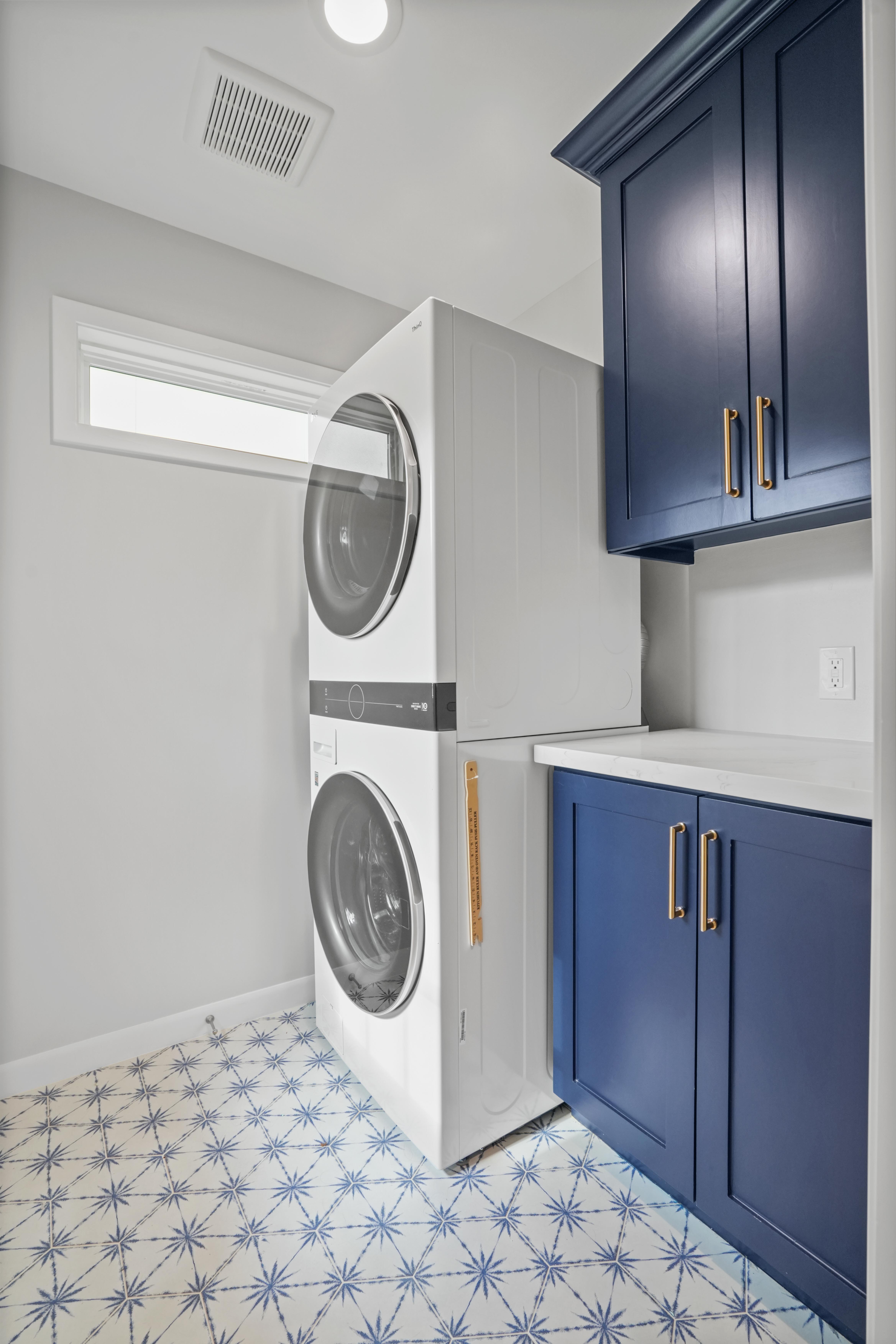 This laundry room is simple and elegant. The navy blue cabinets feature golden handles next to a stacked washer dryer.