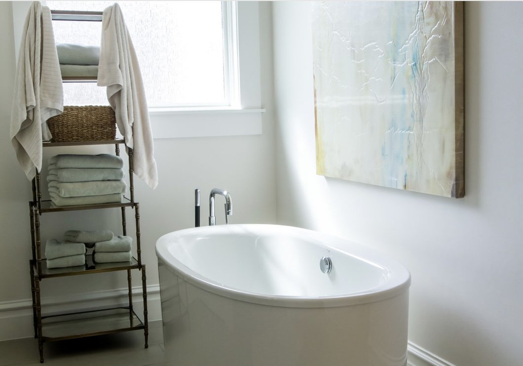 Natural light graces this bathroom with a beautiful. minimal stand alone tub and a shelf with towels at hand.