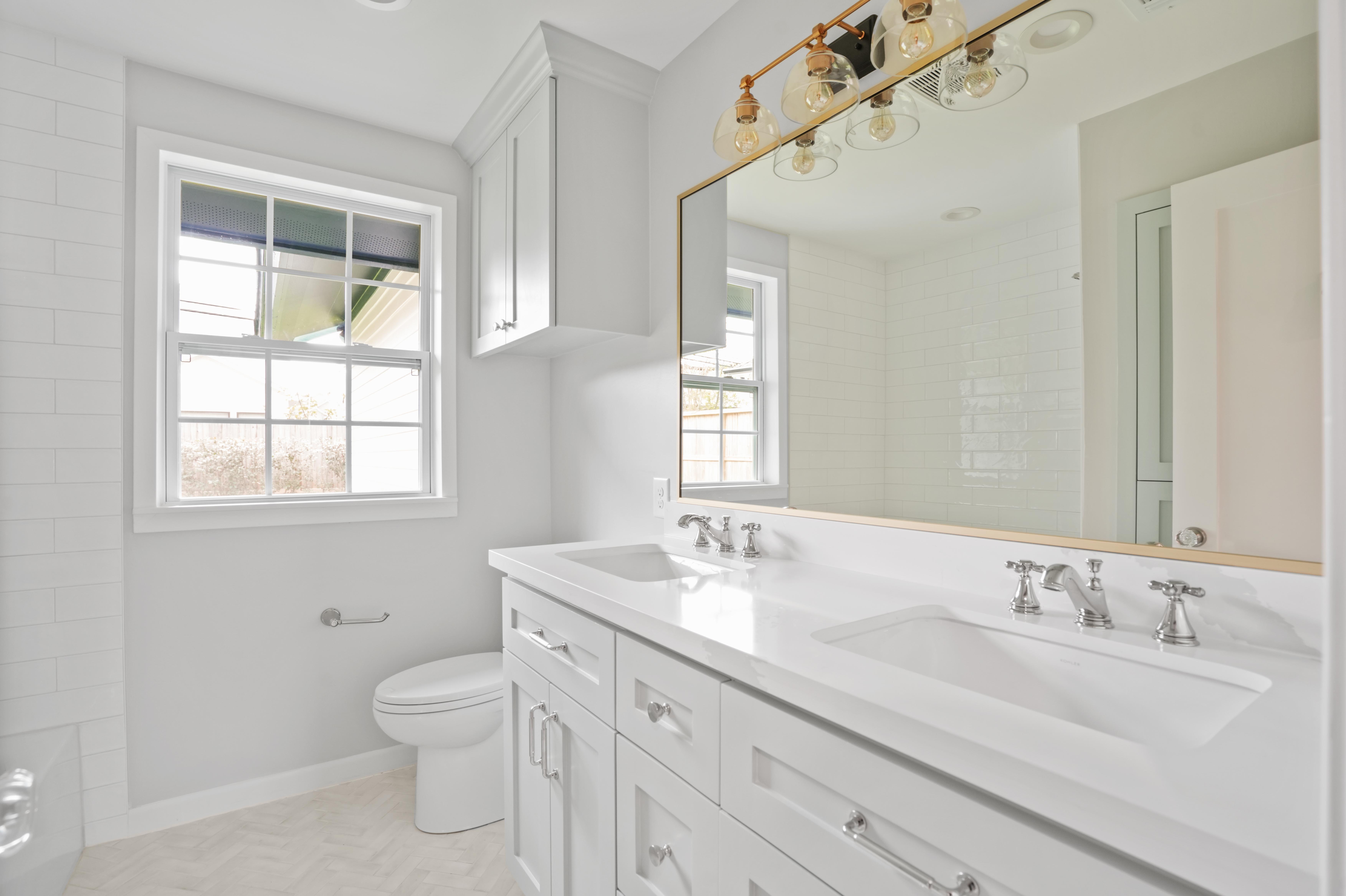 This bathroom is elegant and simple with golden accents around the mirror and light fixtures.