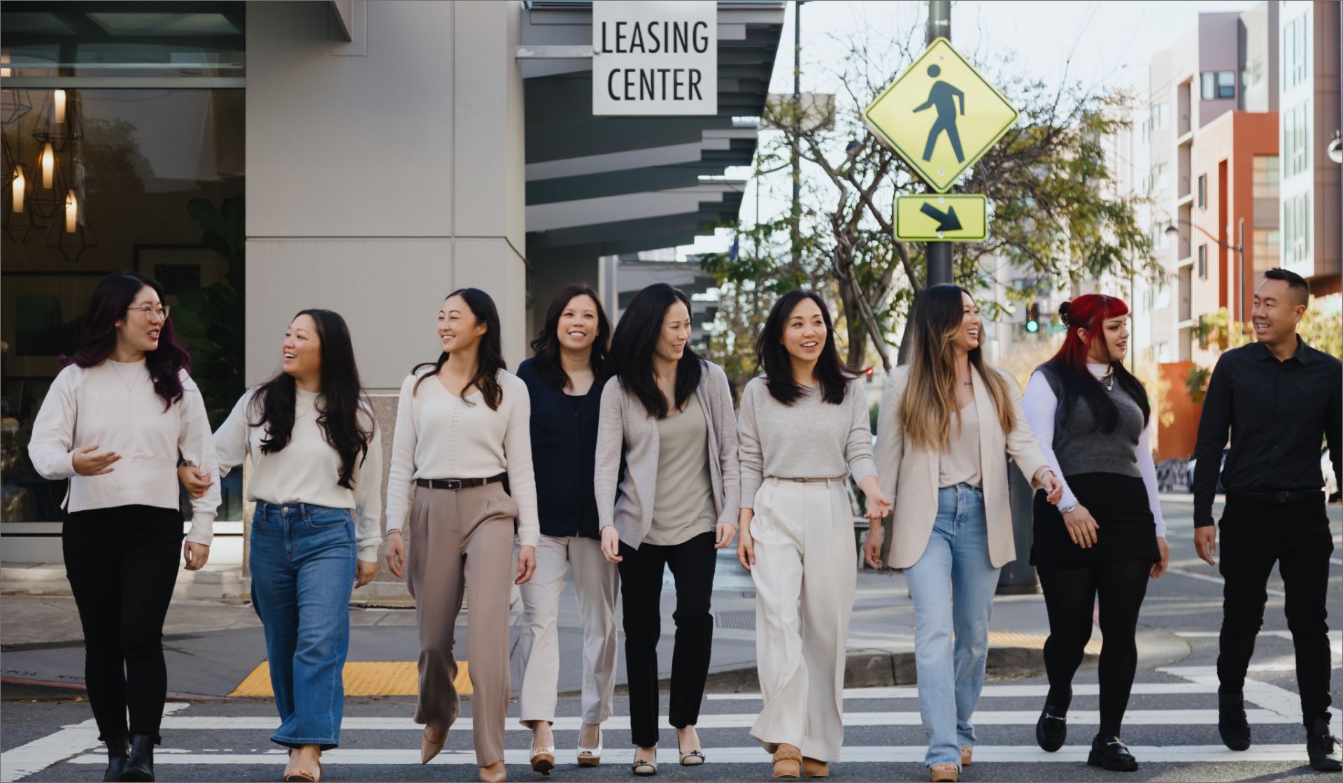 Group of diverse young adults walking together on a city crosswalk, smiling and engaging with each other.