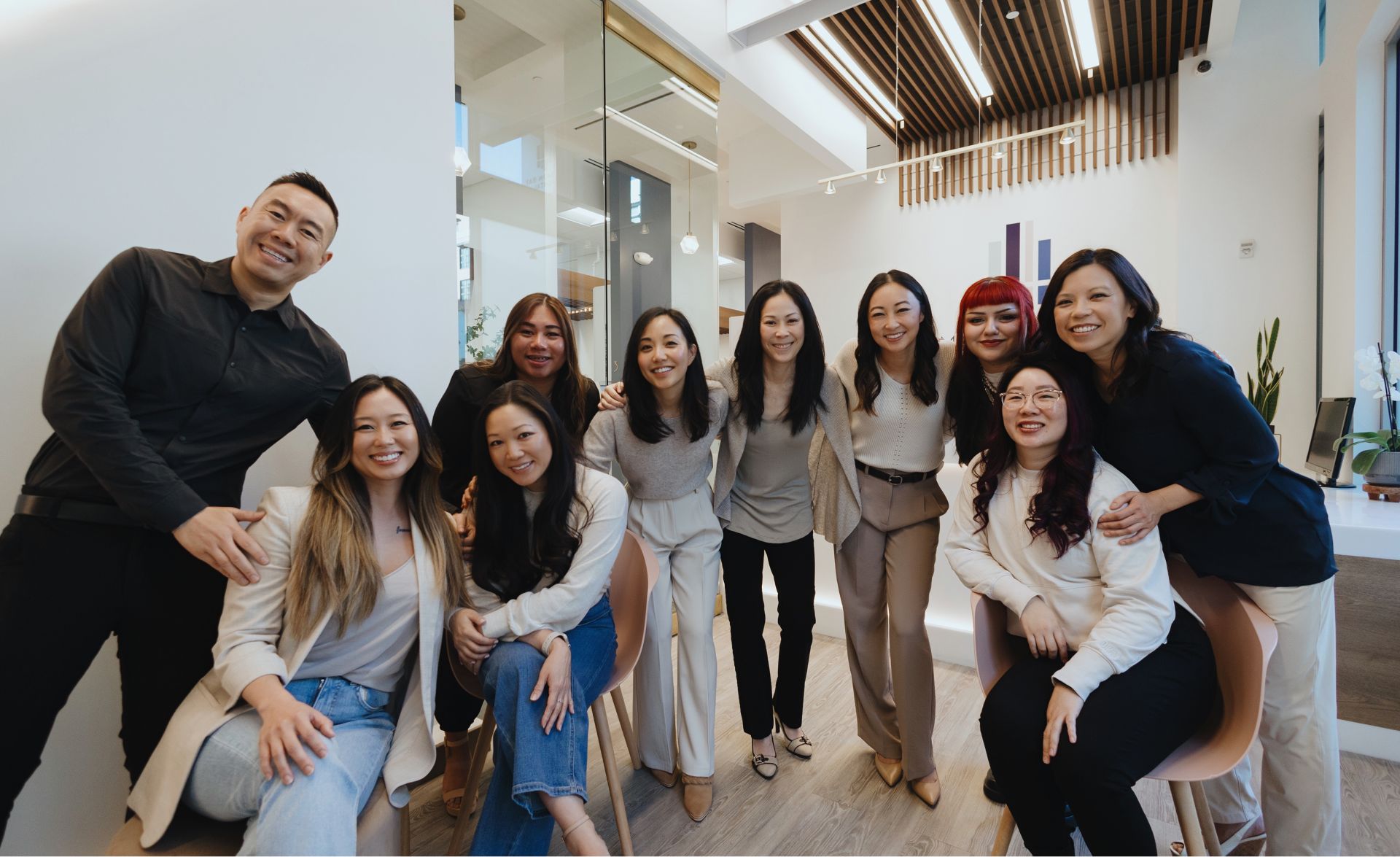 Group of nine people smiling and posing together in a modern office setting.
