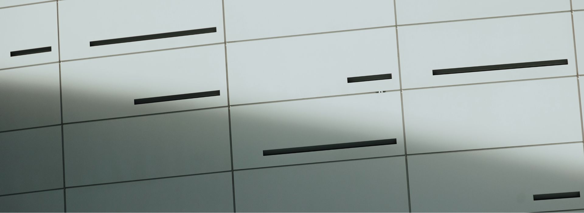 Close-up view of modern building facade with light gray panels and narrow horizontal black windows.