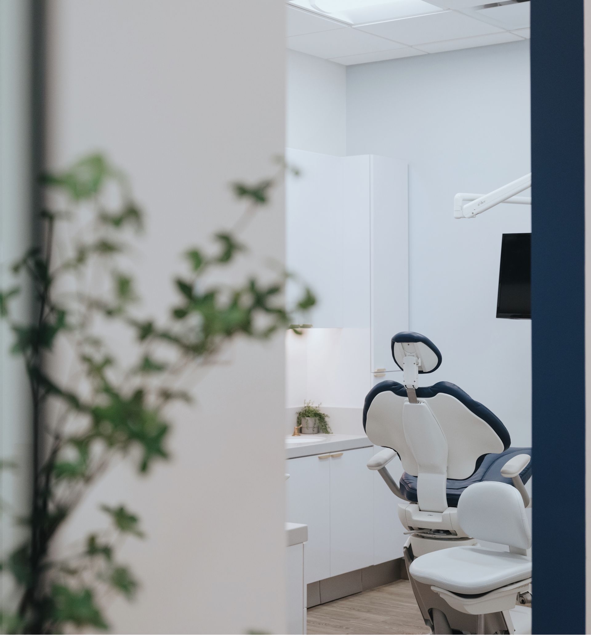 View into a modern dental examination room with a dental chair, white cabinets, and a TV monitor.