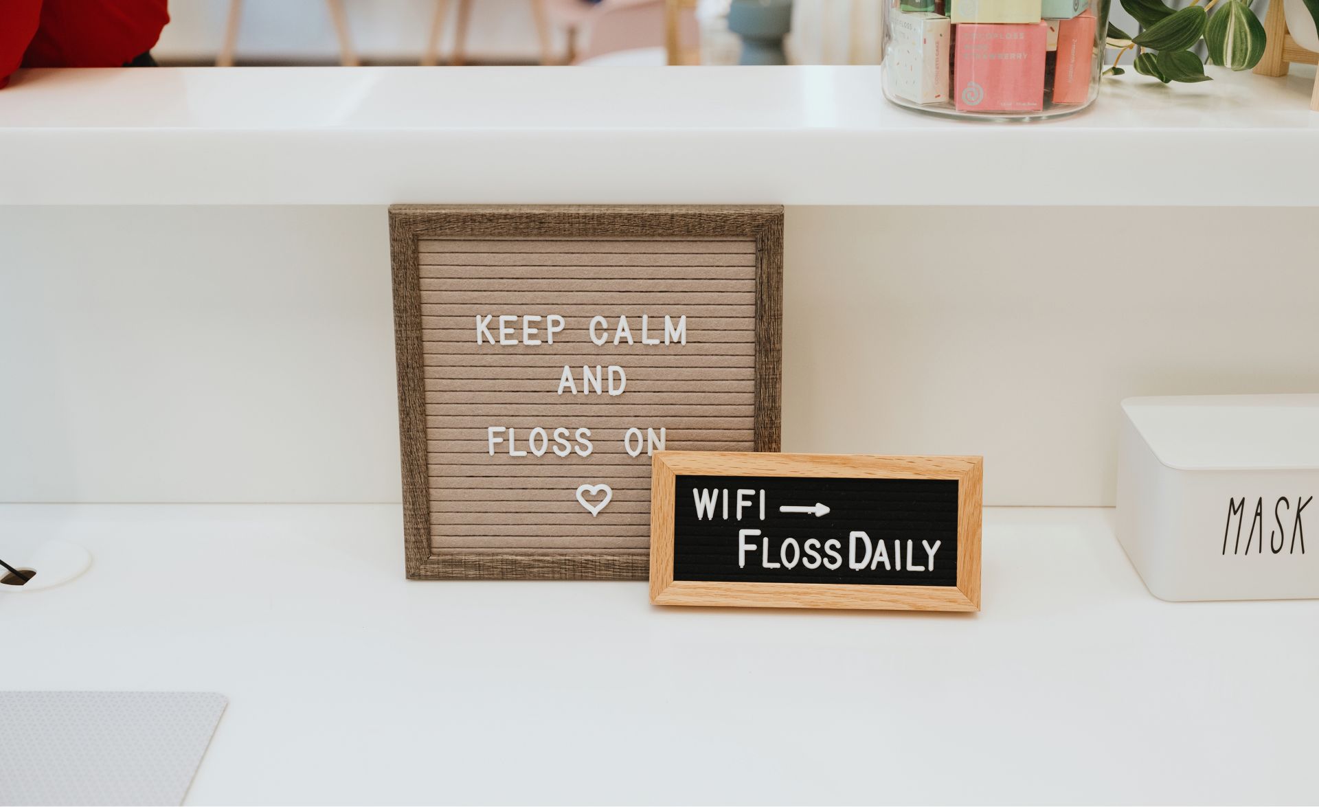 Two letter boards on a white countertop, one says 'KEEP CALM AND FLOSS ON' with a heart symbol, the other says 'WIFI → FLOSS DAILY'.