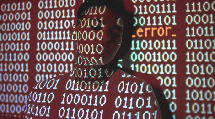 Person with eyes closed standing against a wall with binary code and the word 'error' projected over them.