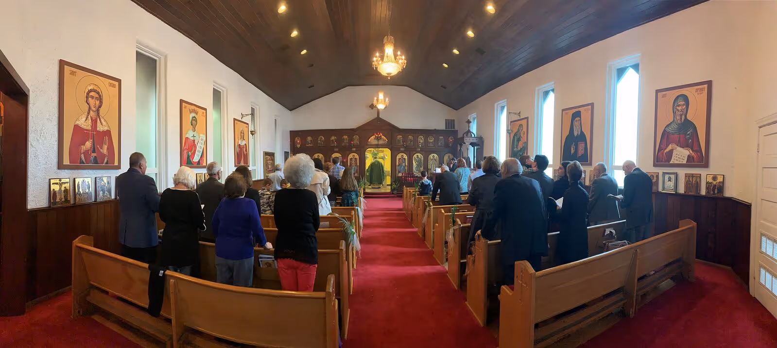 Members of an Orthodox congregation standing in prayer inside a church adorned with traditional icons and liturgical decorations – a moment of communal worship and spiritual reflection.