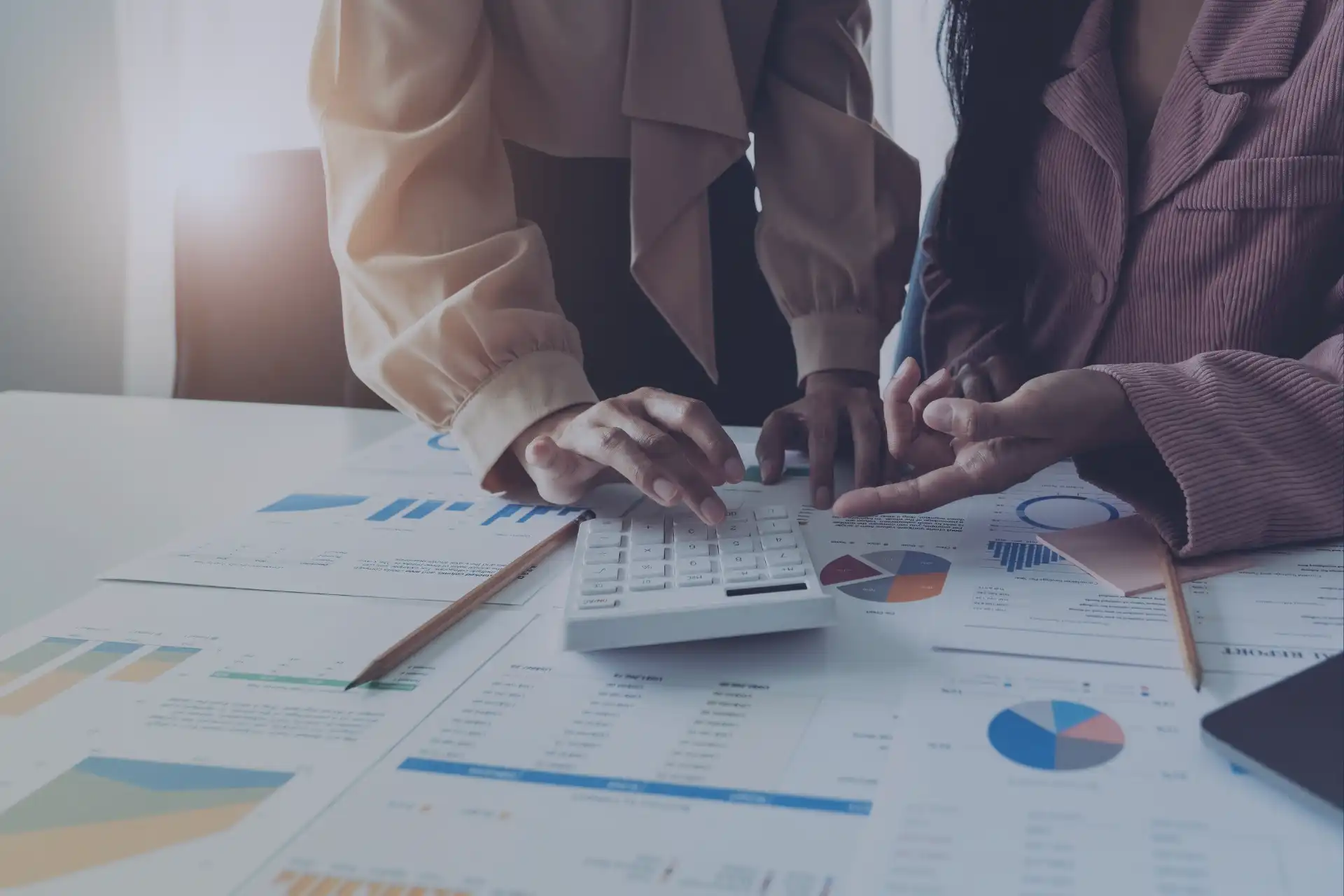 Duas pessoas analisando gráficos e cálculos em um ambiente de escritório, usando uma calculadora e papéis com dados financeiros.
