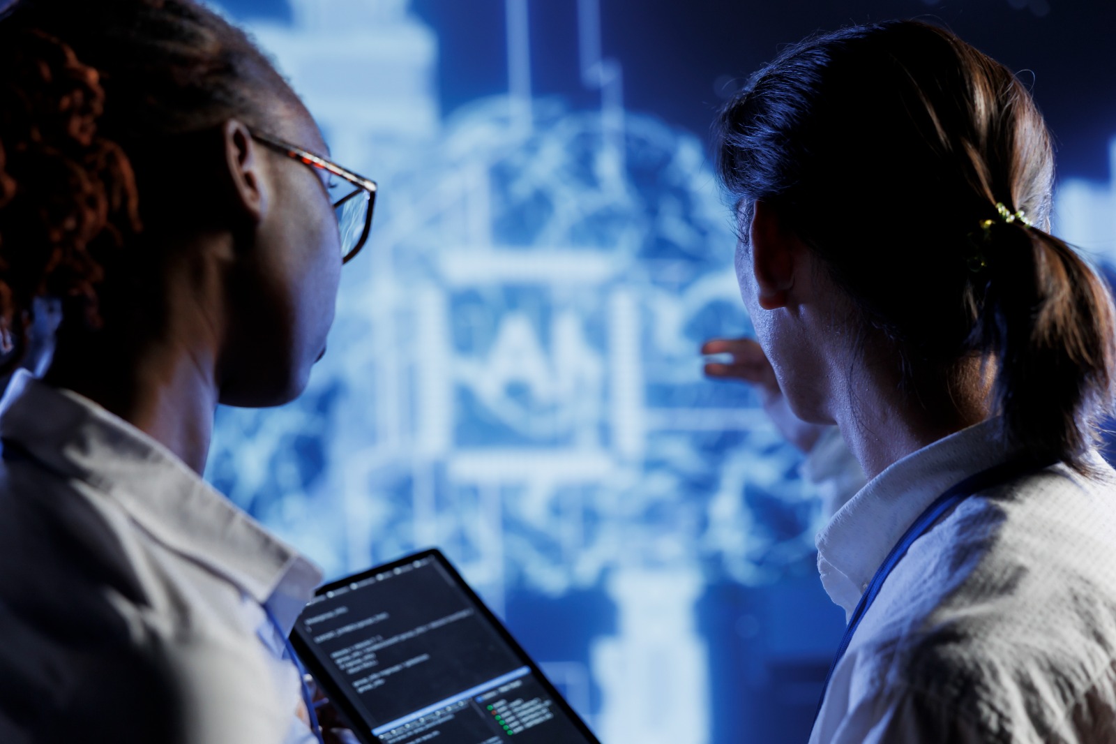 Dupla de profissionais de saúde analisando dados em uma tela digital, possivelmente em um hospital ou laboratório, com foco na tecnologia e inovação na medicina.