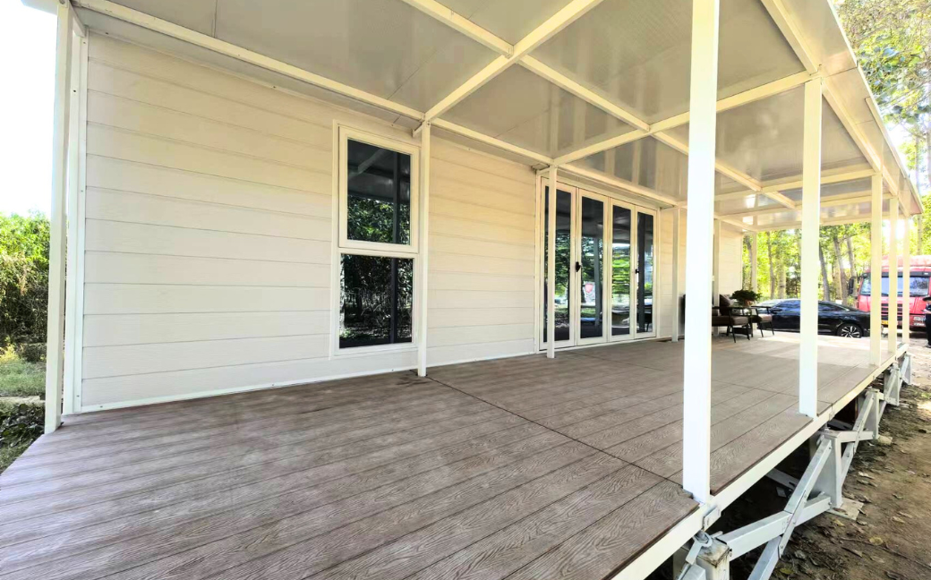 Modern cabin porch with a wooden deck, white railing, and glass sliding doors under a covered roof.