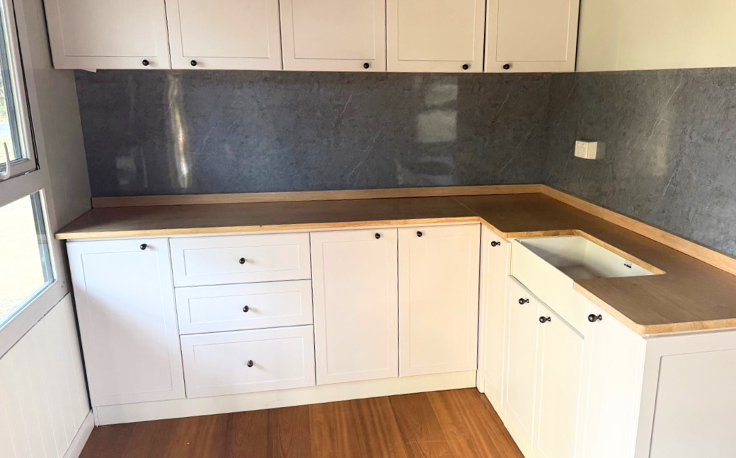 Corner kitchen with white cabinets, wooden countertop, blue-gray backsplash, and a built-in white sink.