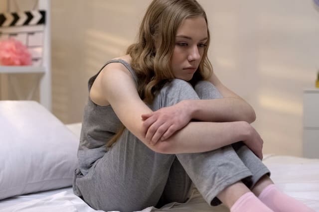 Depressives Mädchen sitzt traurig auf dem Bett
