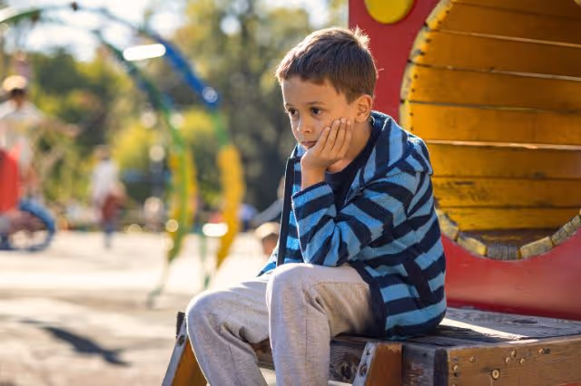 Trauriges Kind sitzt alleine auf dem Spielplatz