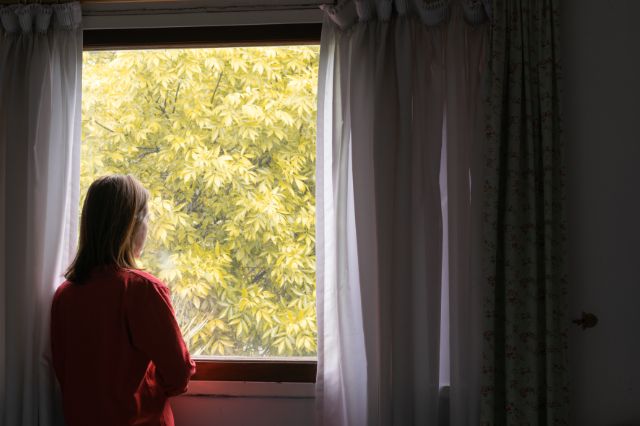Frau steht vor dem Fenster und sieht hinaus