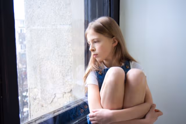 Mädchen sitzt nachdenklich vor dem Fenster