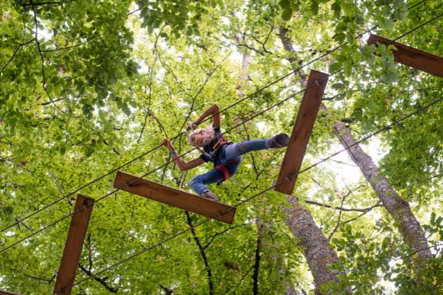  Kind klettert im Hochseilgarten über eine wackelige Holzbrücke