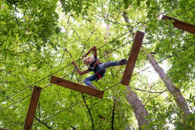  Kind klettert im Hochseilgarten über eine wackelige Holzbrücke