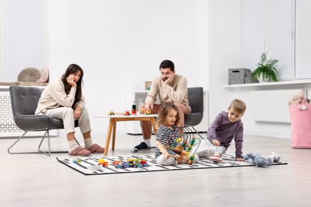 Überforderte Eltern sitzen neben spielenden Kindern