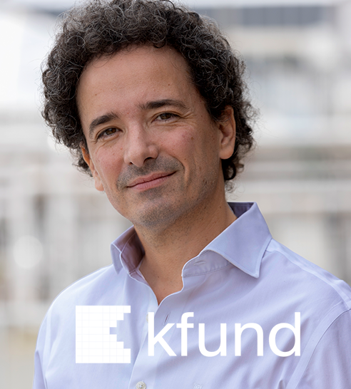 Hombre con cabello rizado y camisa blanca sonriendo, con fondo urbano desenfocado y logo de kfund.
