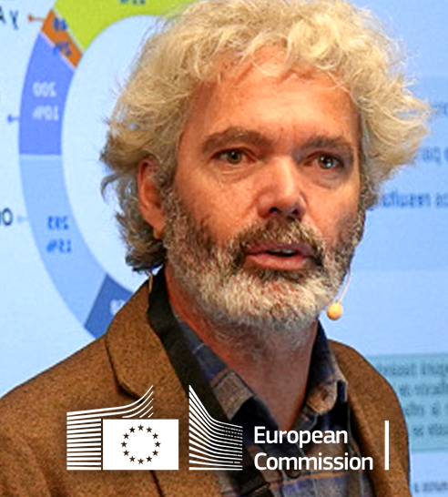 Hombre con cabello y barba canosos hablando frente a una pantalla con gráficos, con el logotipo de la Comisión Europea.