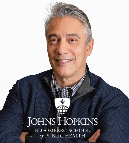 Hombre sonriente con camisa gris claro sobre fondo marrón con logo de Notpla en la esquina inferior izquierda.