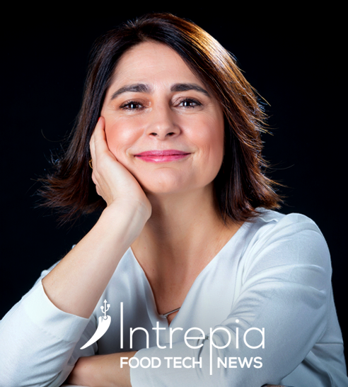 Mujer de cabello corto y oscuro sonriendo, vestida con blazer claro y pendientes de aro.