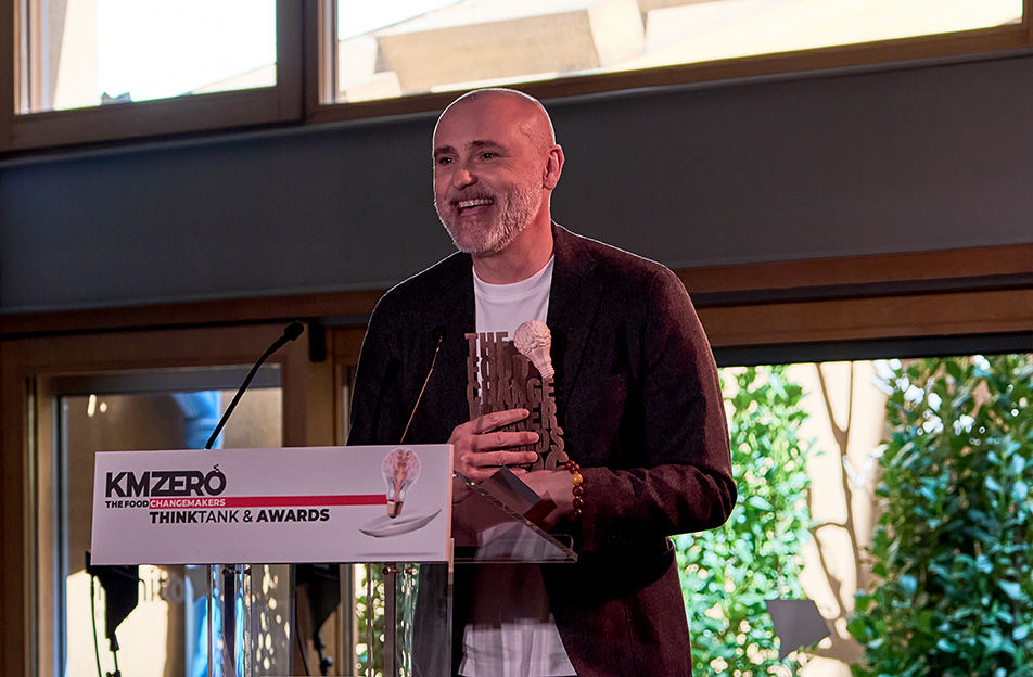 Dos hombres discutiendo documentos sentados en una cafetería, con personas conversando en el fondo.