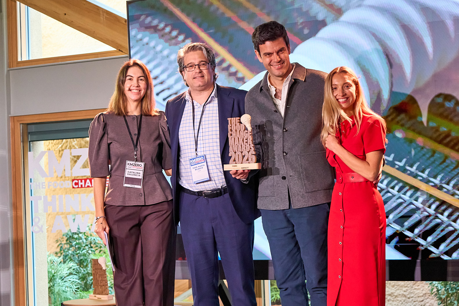 Dos hombres discutiendo documentos sentados en una cafetería, con personas conversando en el fondo.