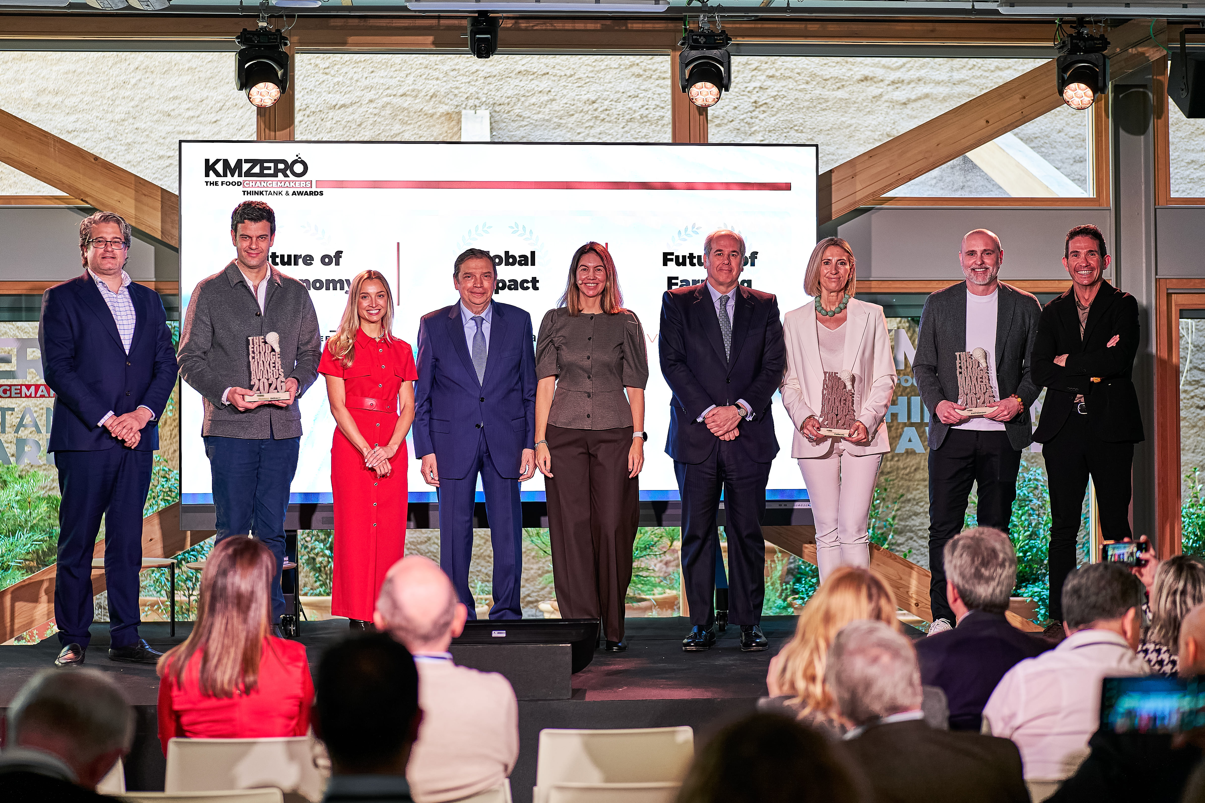 Dos hombres discutiendo documentos sentados en una cafetería, con personas conversando en el fondo.