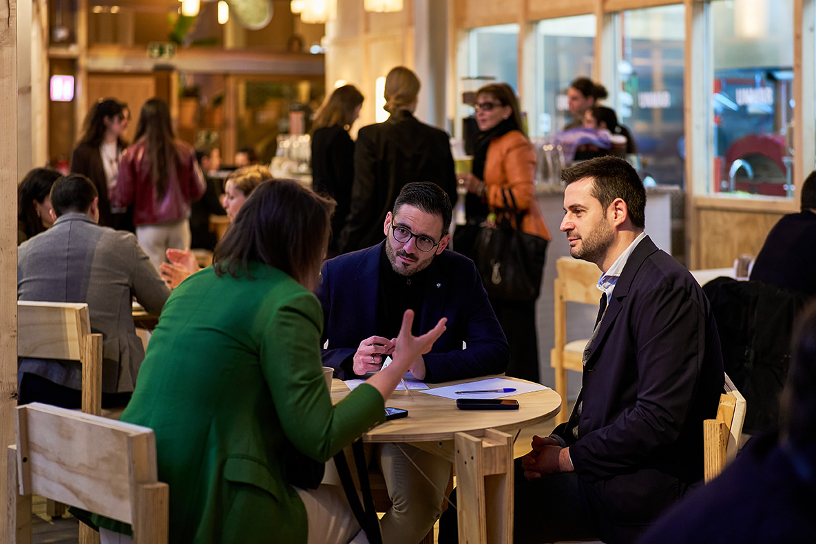 Dos personas conversando en una mesa en un entorno de oficina o reunión.