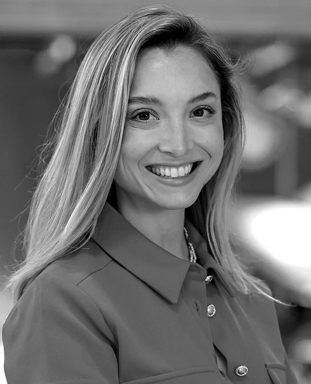 Mujer joven sonriente con cabello largo y suelto, usando un chaleco sin mangas en un fondo con texto desenfocado.