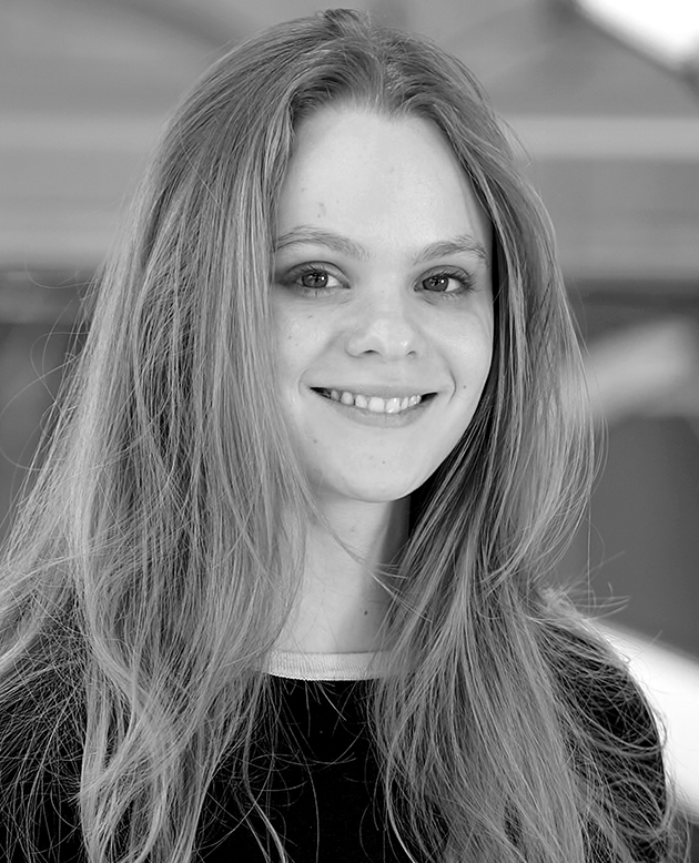 Hombre calvo con camisa negra de manga corta sonriendo con los brazos cruzados en un entorno industrial.