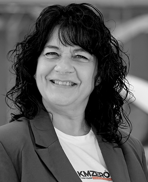 Mujer de mediana edad con cabello rizado y oscuro, sonriendo, vestida con chaqueta de rayas y blusa clara.