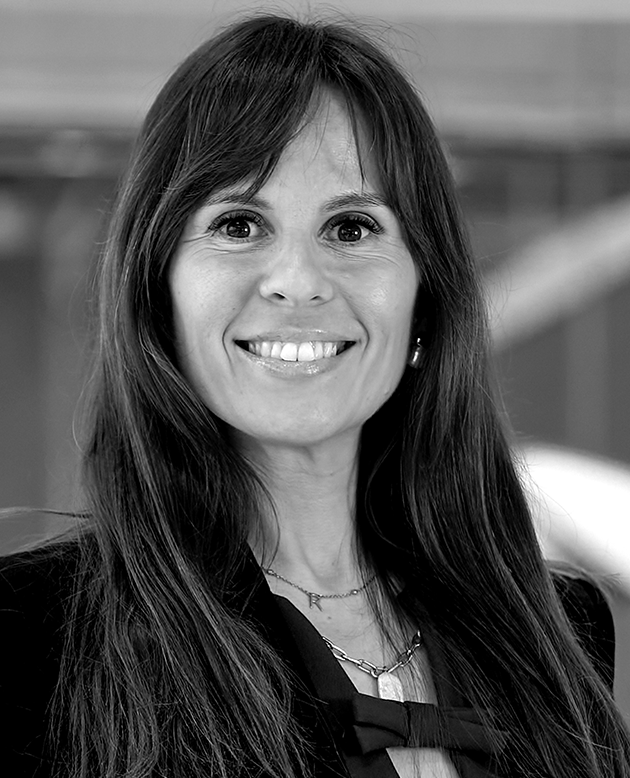 Retrato en blanco y negro de una mujer sonriente con cabello largo y suelto, vistiendo una blusa blanca con detalles tejidos.