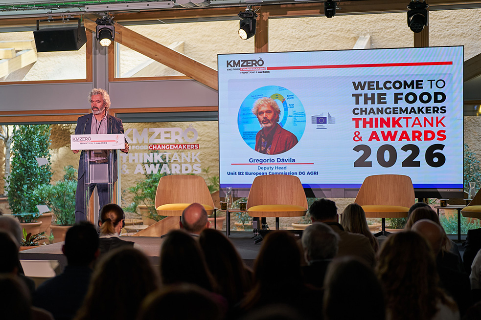 Dos hombres sentados en una mesa redonda discutiendo mientras uno usa gestos con las manos y frente a una tablet.