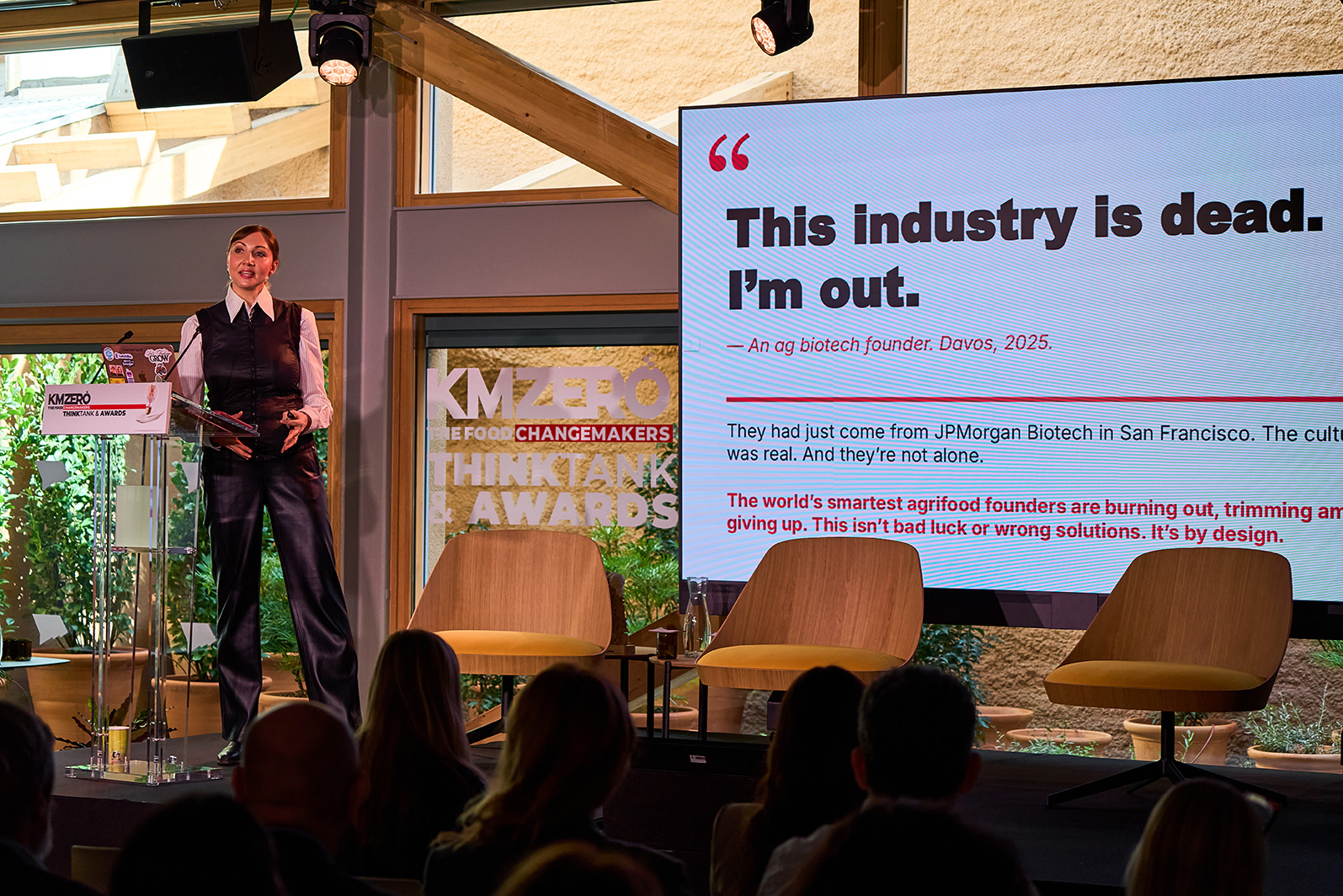 Dos hombres sentados en una mesa redonda discutiendo mientras uno usa gestos con las manos y frente a una tablet.