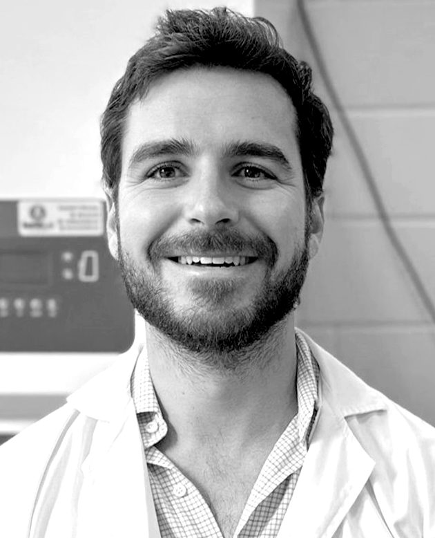 Hombre sonriendo con los brazos cruzados, vestido con chaqueta oscura y camisa blanca.