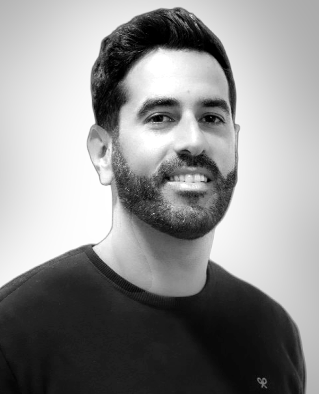 Hombre sonriendo con los brazos cruzados, vestido con chaqueta oscura y camisa blanca.
