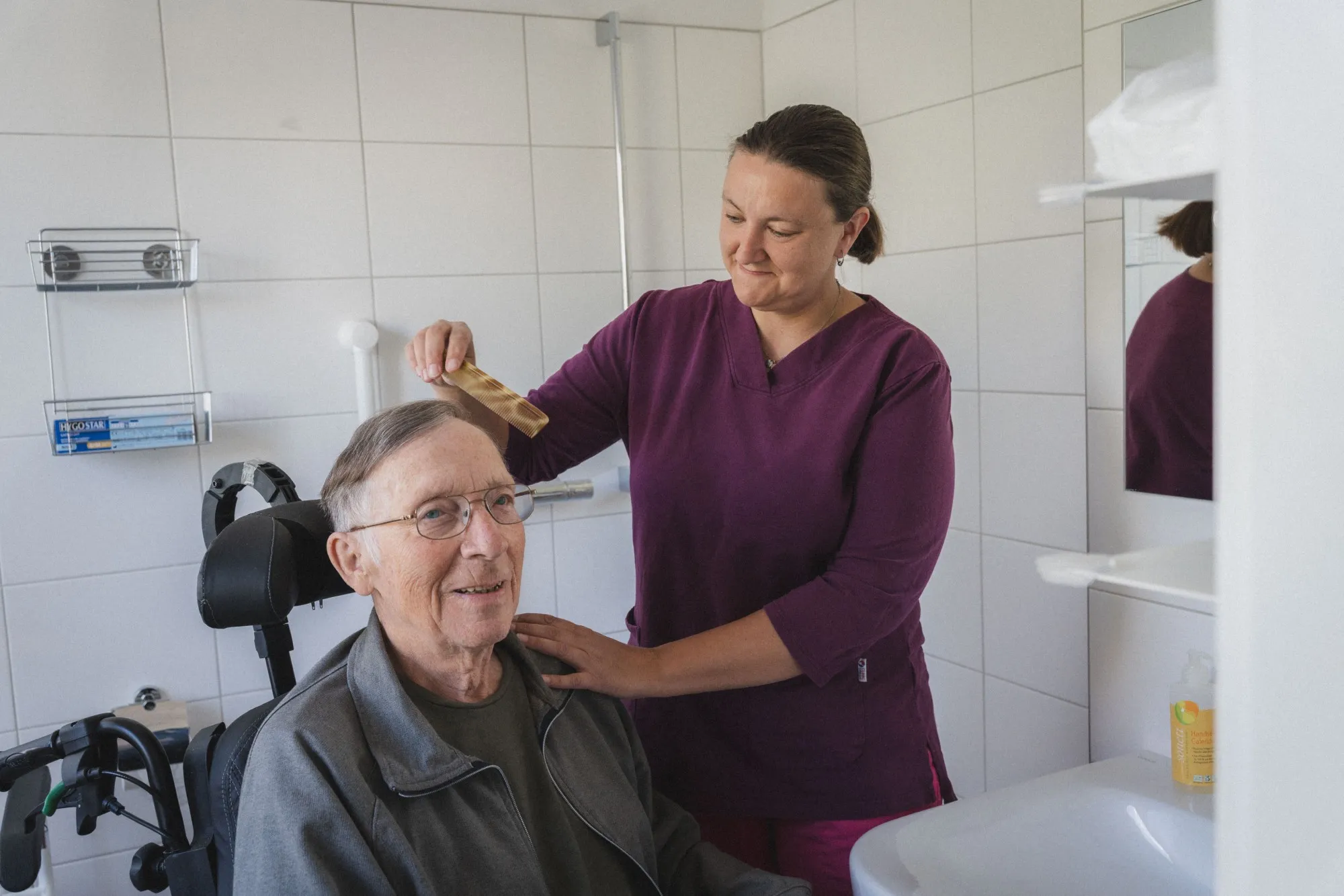 Häusliche Krankenpflege - Pflegerin kämmt einen Mitbewohner.