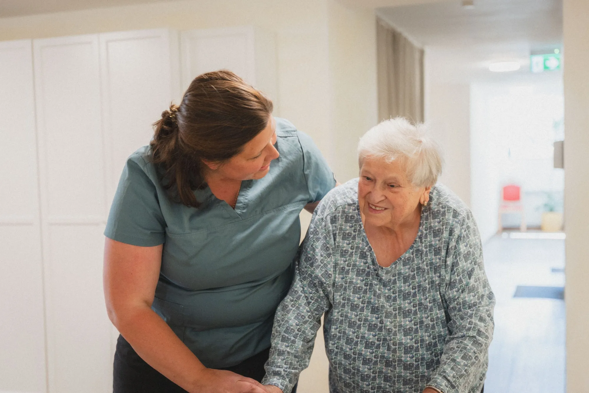 Mitarbeiterin des Pflegedienstes lebenswert hilft einer Bewohnerin beim gehen.