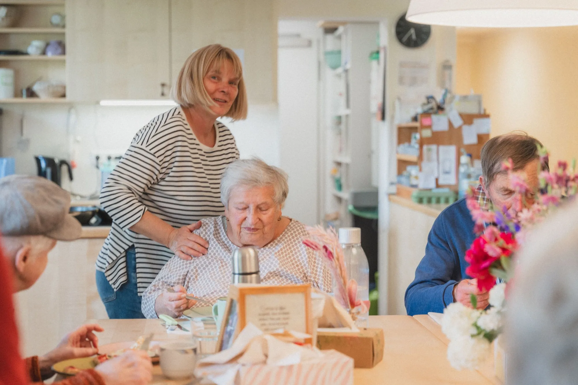 Mitarbeiter:innen am Esstisch in der Wohngemeinschaft mit Bewohnern.